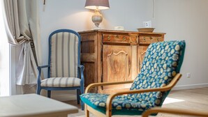 A room with a wooden cabinet, a striped chair, a patterned armchair, and a table.