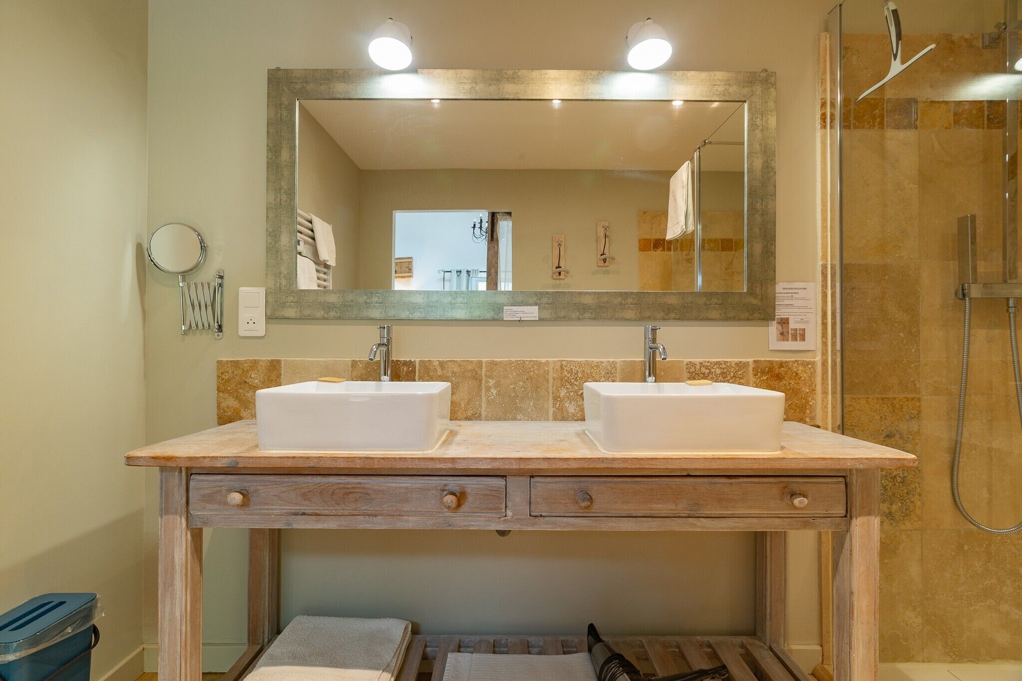 Un bagno con due lavandini, uno specchio, una doccia e un mobile contenitore in legno.