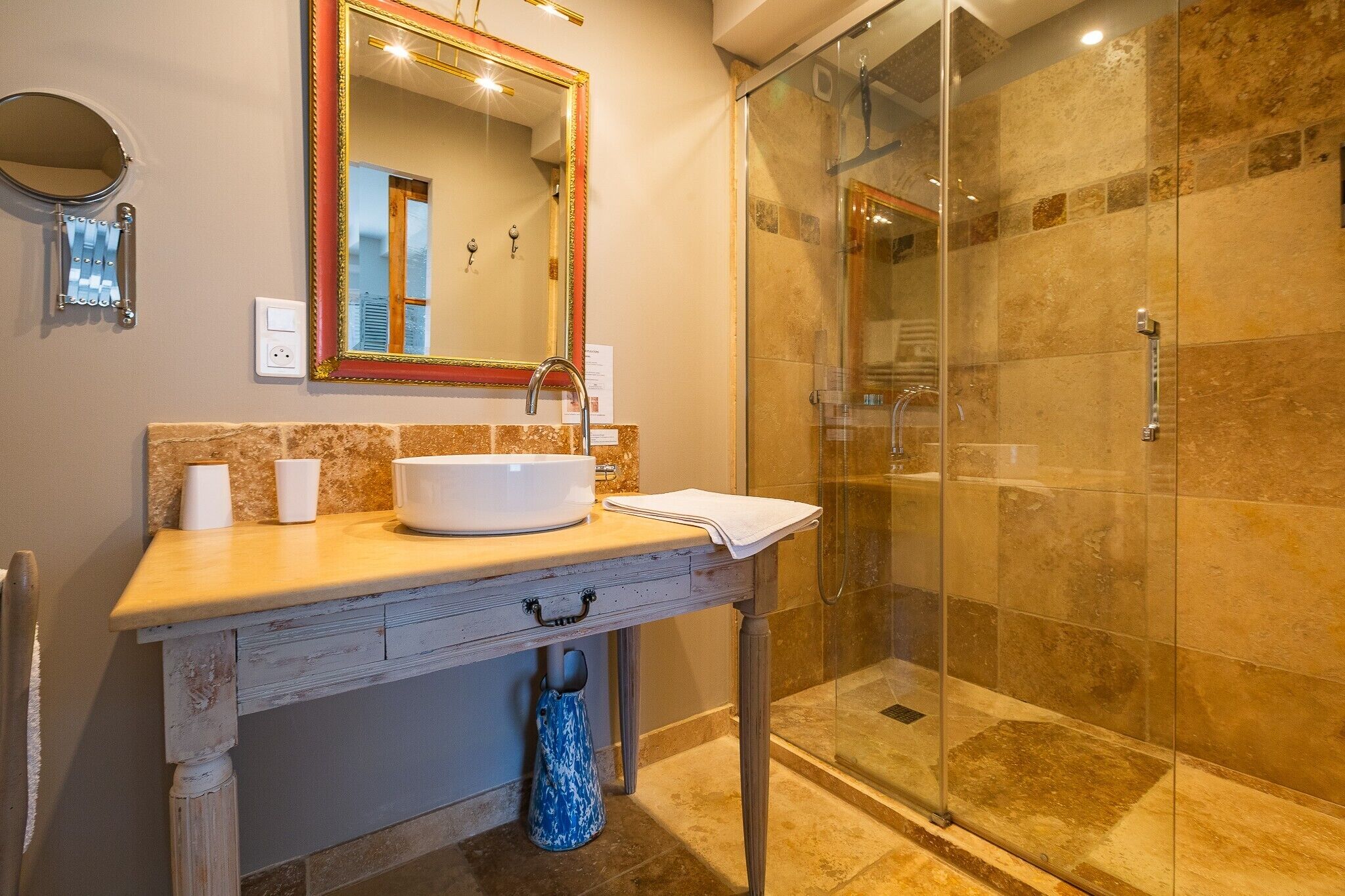 Een badkamer met een douchecabine van glas, een wit wastafelmeubel en een spiegel met gouden lijst.