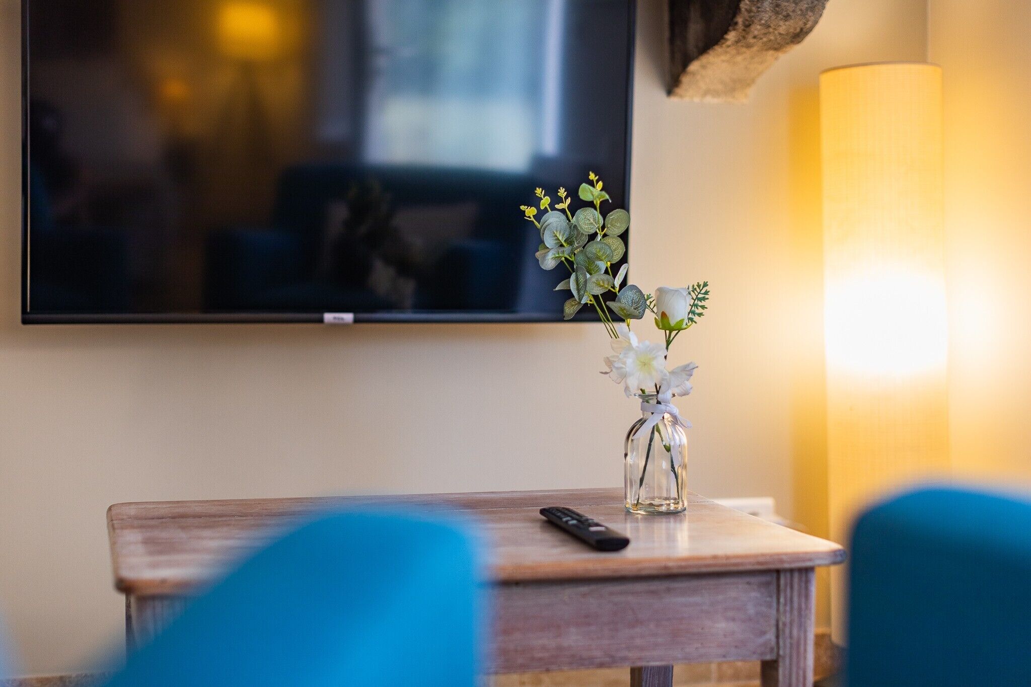 Ein Hotelzimmer mit Holztisch, Blumenvase, Fernbedienung und Fernseher an der Wand.