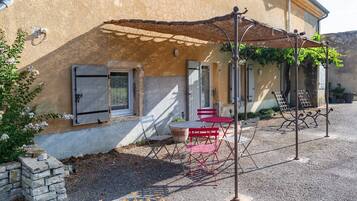 Un edificio con pared de piedra, una mesa y sillas rojas, y una pérgola de metal.