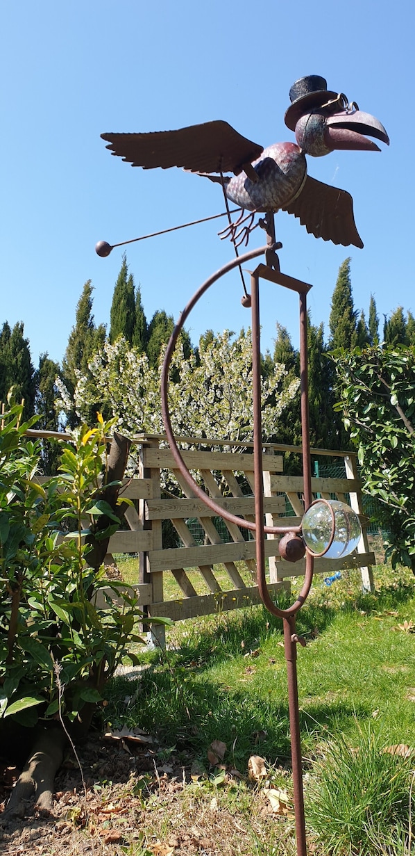 Une sculpture métallique en forme d’oiseau, dotée d’ailes et d’une queue, montée sur un poteau surmonté d’un miroir circulaire.