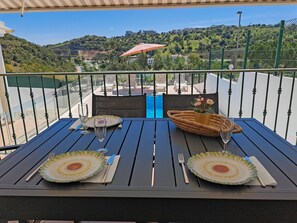 Une table dressée pour deux personnes, avec des assiettes, des couverts et un verre, sur un balcon donnant sur un paysage magnifique.