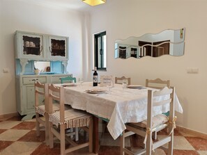 Un coin repas avec une table dressée pour quatre personnes, un buffet bleu aux portes vitrées, un miroir au mur et une fenêtre donnant sur un beau paysage.
