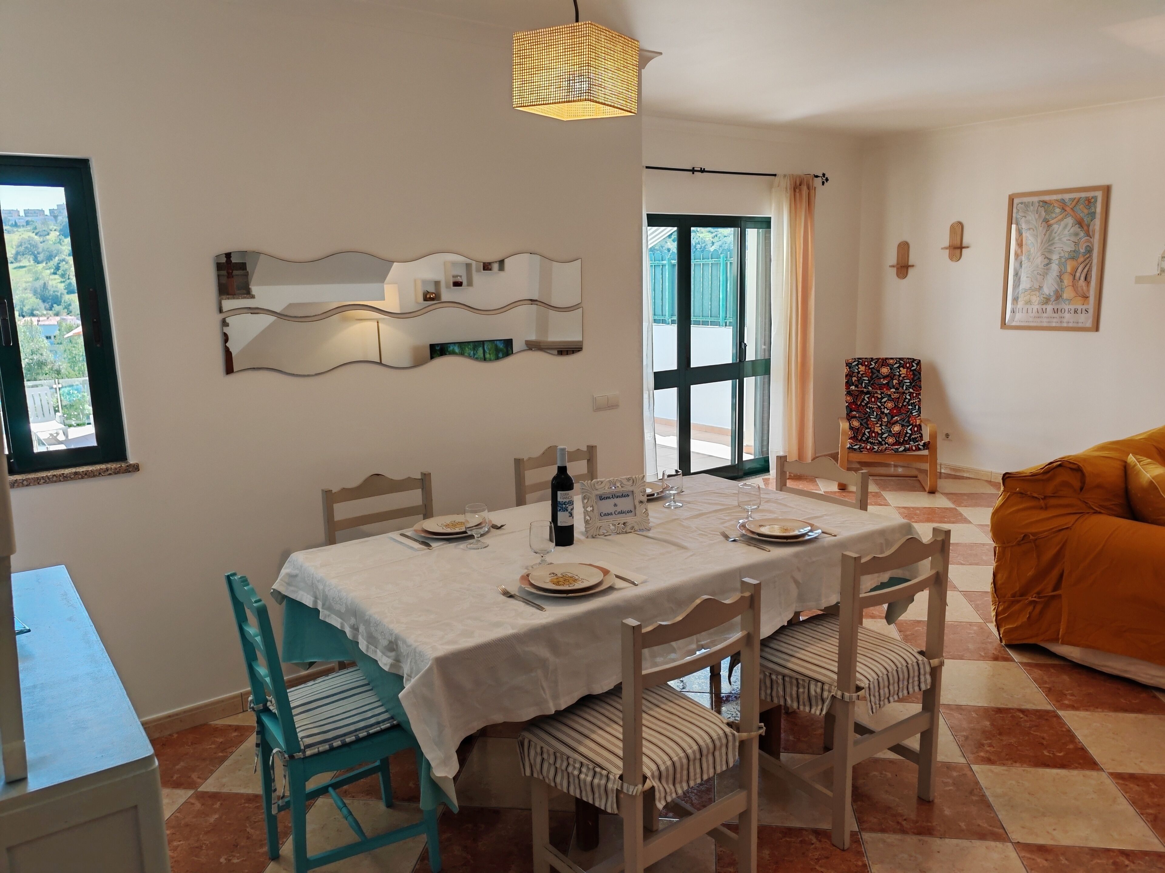 Comedor con una mesa dispuesta para cuatro, sillas, una botella de vino y un cartel que dice 'Welcome to Villa Calendas'.
