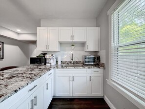 A compact kitchen with white cabinets, a granite countertop, a microwave, a coffee maker, and a toaster. - Riverside Heights 2BR/1BA Tampa | Balcony & Parking (Tampa)