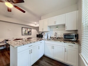 A kitchen with white cabinets, a granite countertop, a ceiling fan, and a microwave. - Riverside Heights 2BR/1BA Tampa | Balcony & Parking (Tampa)
