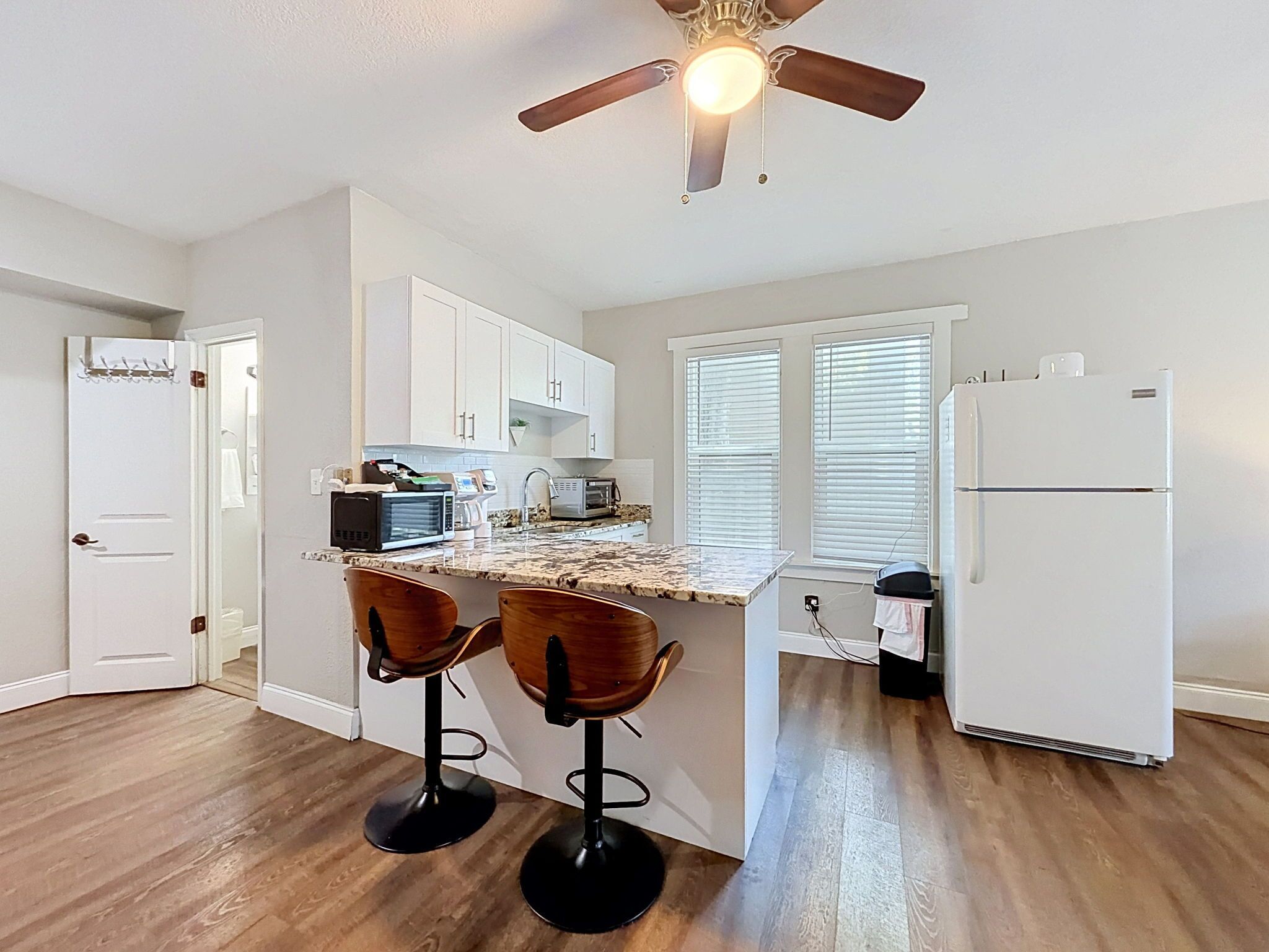 A kitchen with a central island, two bar stools, a ceiling fan, and a refrigerator.