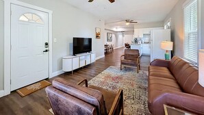 A living room with a television, a brown leather sofa, a brown leather chair, a dining area, and a kitchen in the background. - Tampa Heights 2BR Near Riverwalk (Tampa)