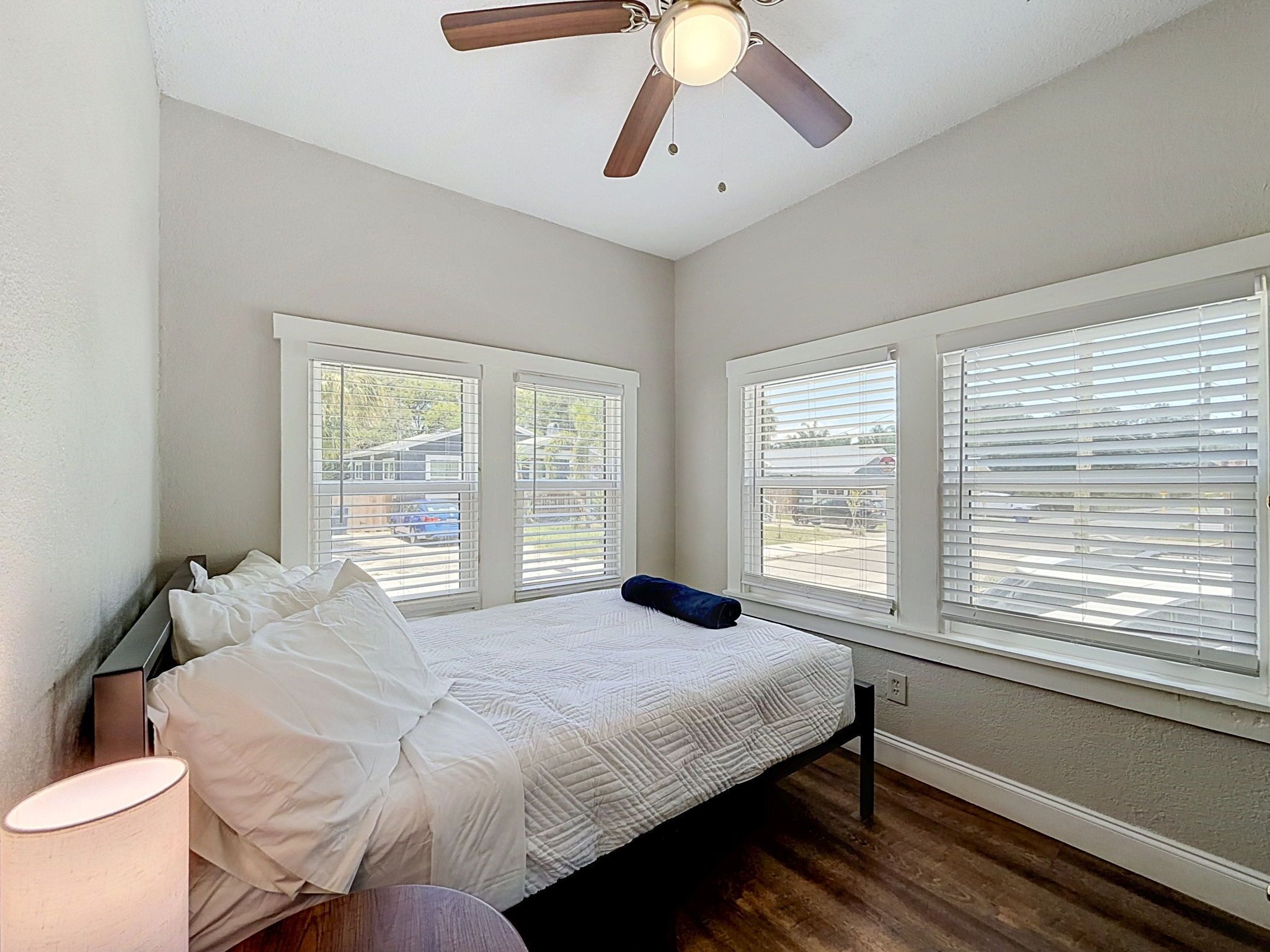Un dormitorio con una cama, un ventilador de techo y tres ventanas con persianas.