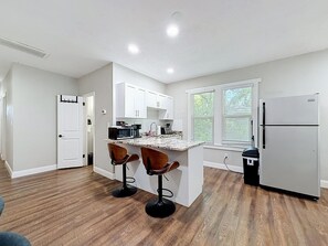A modern kitchen with white cabinets, a granite countertop, and two bar stools. - 2BR Tampa Heights Apartment with Balcony & Parking (Tampa)