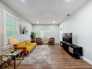 Ein Wohnzimmer mit einer Couch, Sesseln, einem Couchtisch, einem Fernseher und einer Pflanze.