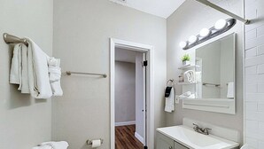 Un bagno con il water, un lavandino, uno specchio, un portascopevoli e una porta che dà su un'altra stanza.