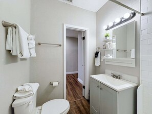 Ein Badezimmer mit Toilette, Waschbecken, Spiegel, Handtuchhalter und einer Tür zu einem anderen Raum.