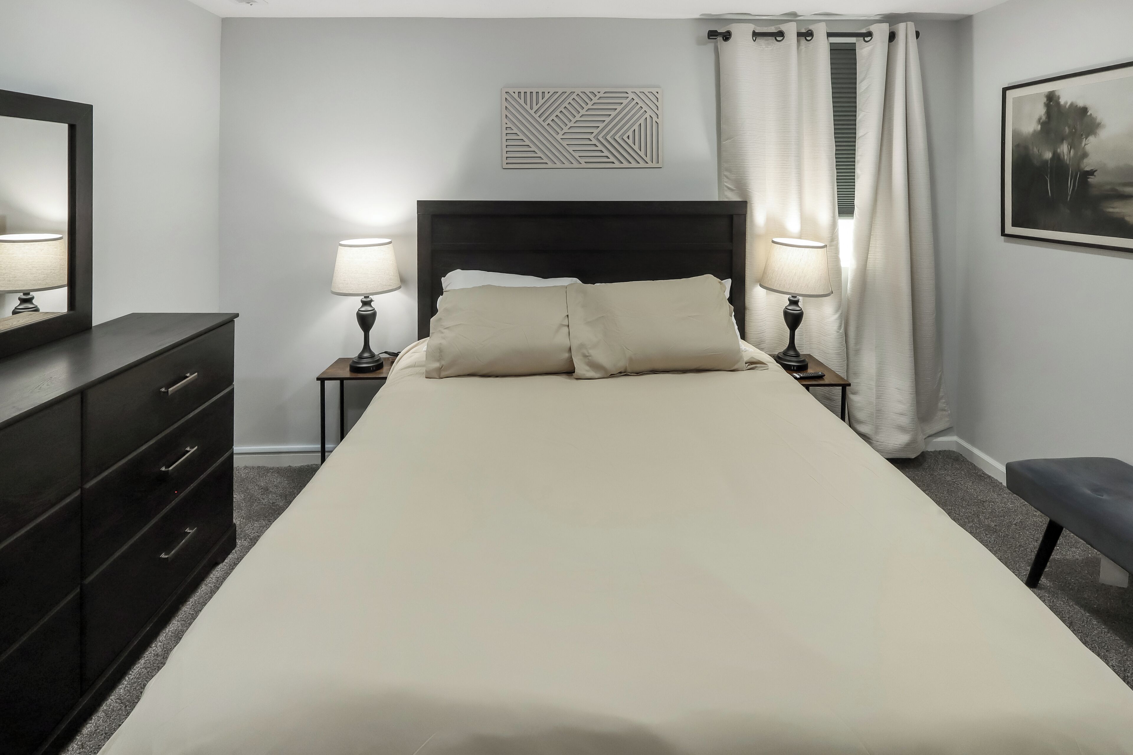 Een slaapkamer met een bed, twee bedlampen, een hoofdeinde, een kaptafel, een bankje en een schilderij aan de muur.