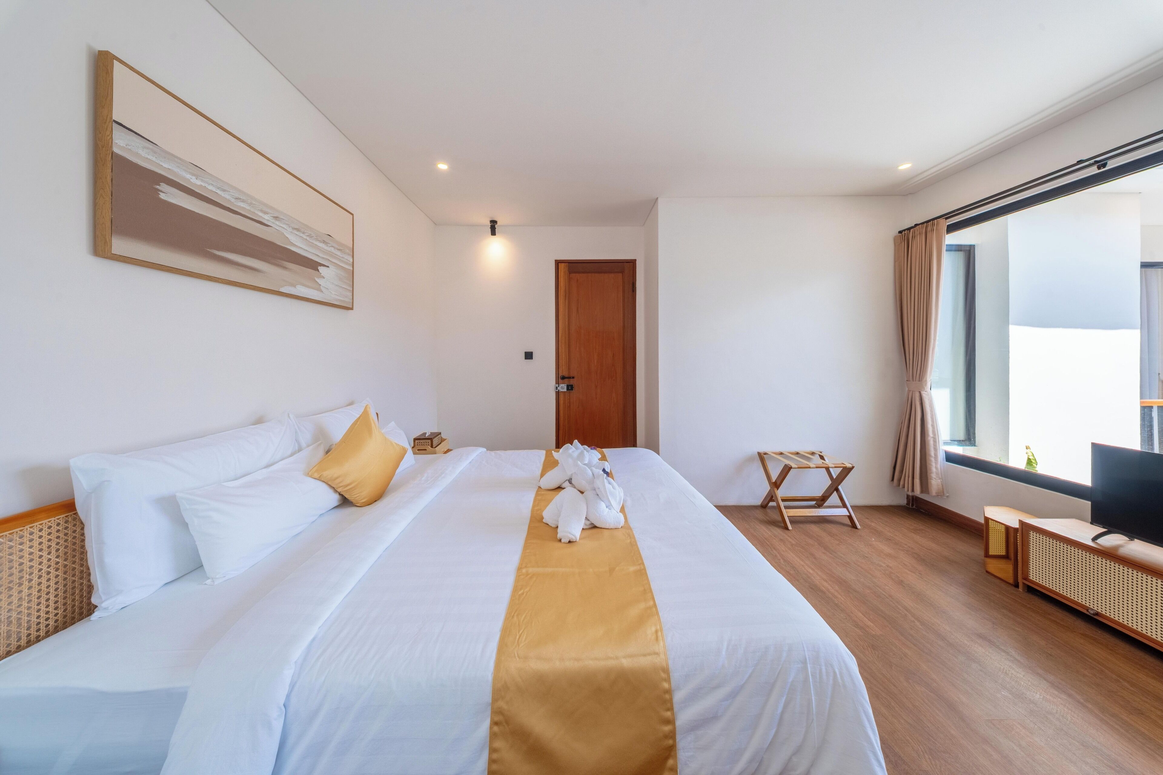 A hotel room with a large bed, a television, a window with curtains, and a wooden floor.