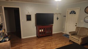 A living room with a flat-screen TV on a wooden cabinet, a door with a window, and a wall-mounted clock. - Cozy 2-bedroom house in charming Clarksville with AC (Clarksville)