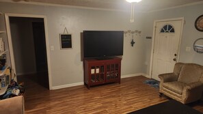 Ein Wohnzimmer mit Flachbildfernseher auf einem Holzschrank, einer Tür mit Fenster und einer Wanduhr.