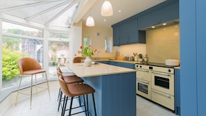 A modern kitchen with a large island, blue cabinets, and a view to the outside. - Number eight - sleeps 8 guests  in 4 bedrooms (Beaumaris)