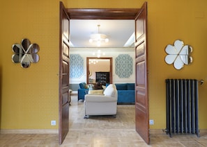 A hallway leading to a living room with patterned wallpaper, a blue sofa, a patterned armchair, and a chandelier. - Holiday Home 'Villa Almudena' with Private Pool, Wi-Fi and Air Conditioning (Nava de la Asunción)