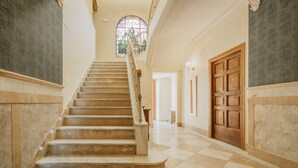 A grand staircase with marble steps and a wooden handrail, leading to a door with a large window above.