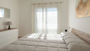 Una camera da letto con un letto, un comodino, una lampada, una finestra con tende e un'opera d'arte appesa al muro.