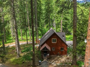 A cabin surrounded by tall trees, with a gravel driveway leading to the entrance. - Mountain Cabin w/ Hot Tub - Sleeps 6 (Peshastin)