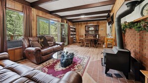 A cozy living room with leather sofas, a glass coffee table, a fireplace, and a dining area with wooden furniture. - Mountain Cabin w/ Hot Tub - Sleeps 6 (Peshastin)