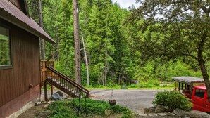 A cabin with a wooden exterior, a gravel driveway, a fire pit, and a red vehicle parked nearby. - Mountain Cabin w/ Hot Tub - Sleeps 6 (Peshastin)