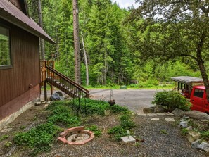 A cabin with a wooden exterior, a gravel driveway, a fire pit, and a red vehicle parked nearby. - Mountain Cabin w/ Hot Tub - Sleeps 6 (Peshastin)