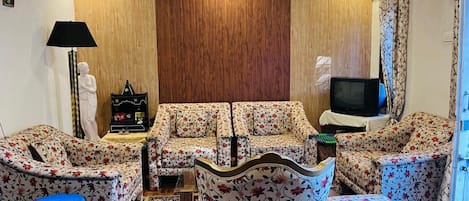 A living room with a sofa set, a television, a lamp, and a small statue.