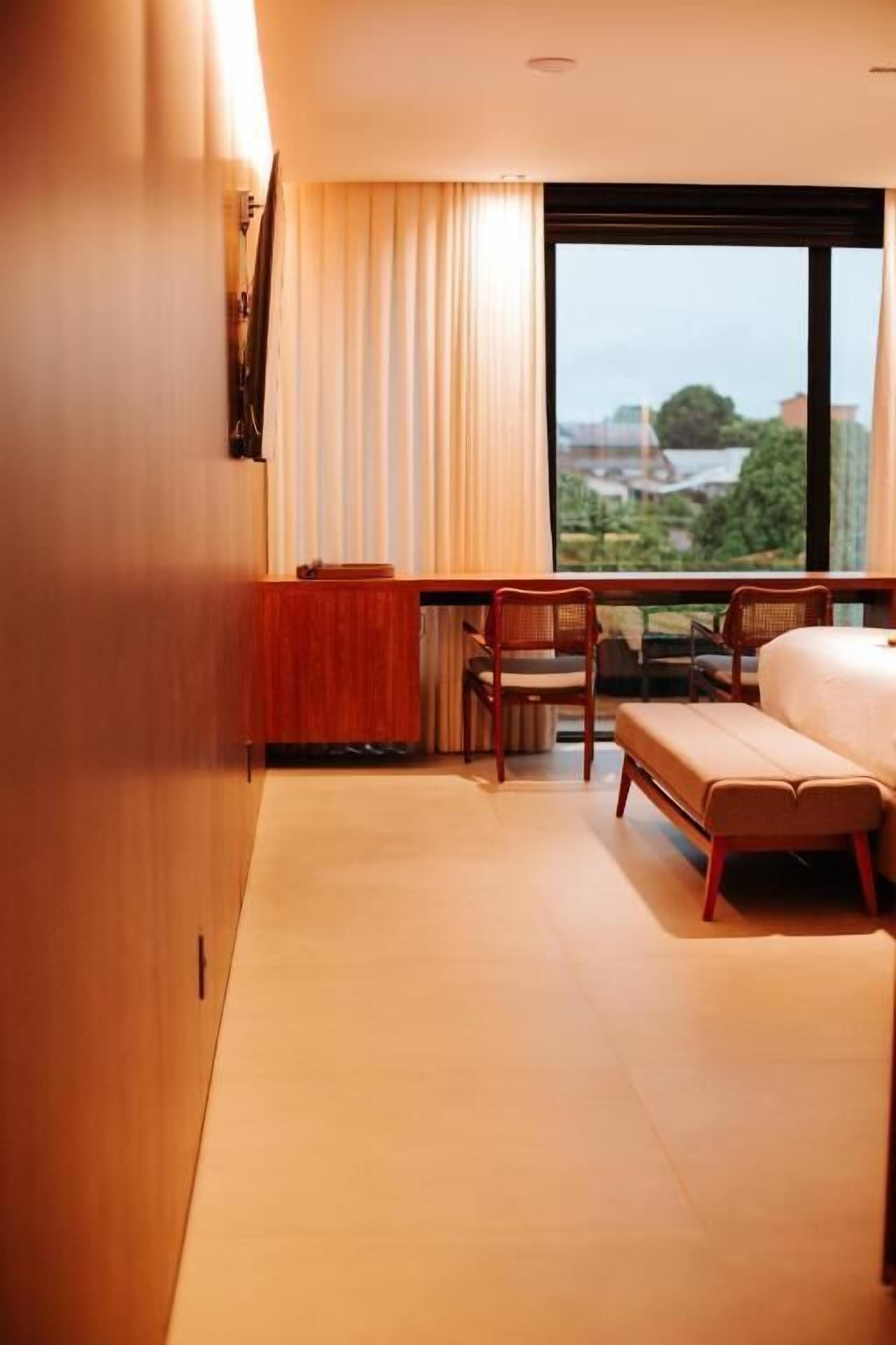 A hotel room with a bed, two chairs, a small table, and a large window with a view.
