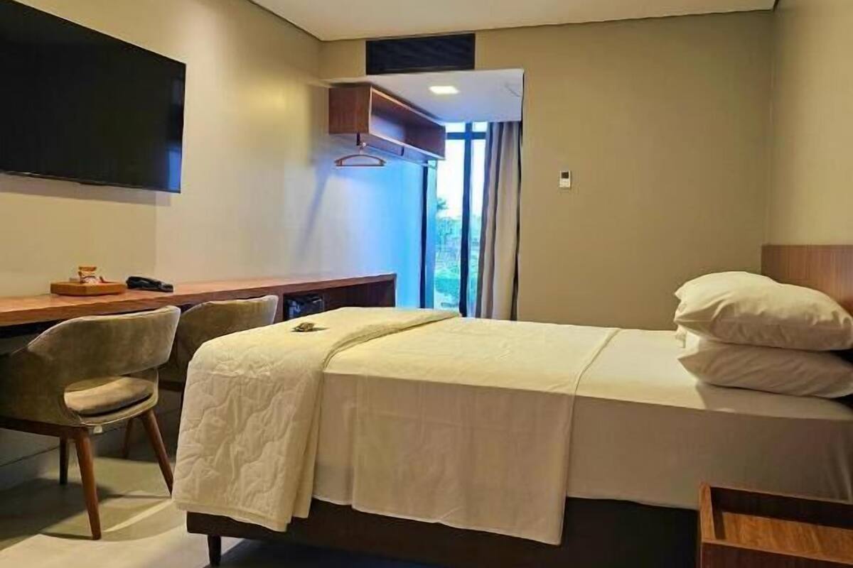 A hotel room with a bed, a desk, a chair, and a TV.