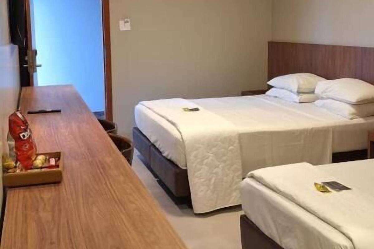 A hotel room with two beds, a wooden desk, and a door leading to a bathroom.