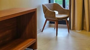 Una habitación moderna con un aparador de madera, un sillón curvo y un amplio ventanal con cortinas.
