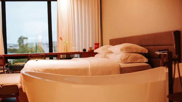 Una habitación de hotel con cama, una silla, un escritorio y una ventana con cortinas.
