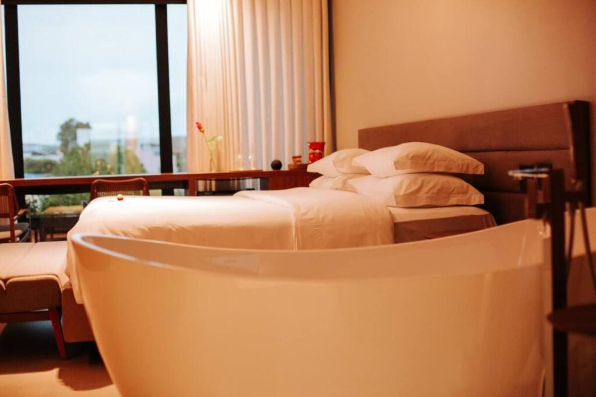 A hotel room with a bed, a chair, a desk, and a window with curtains.