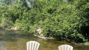 Två Adirondack-stolar står i en grund flod, omgivna av tät vegetation.