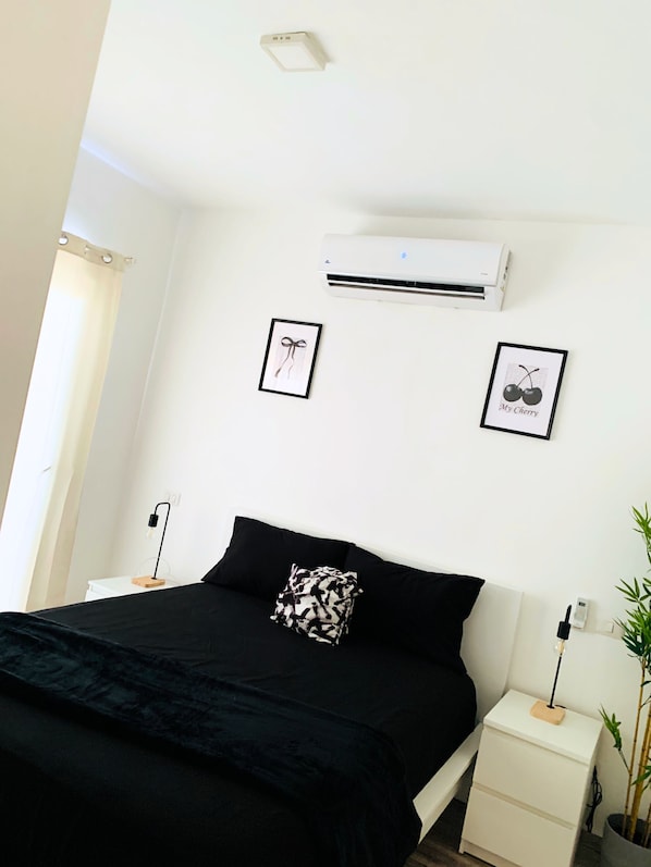 Ein Schlafzimmer mit einem Bett, einem Nachttisch, einer Wand-Klimaanlage und zwei gerahmten Bildern.