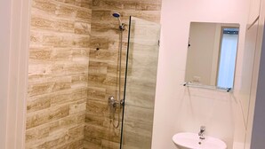Ein modernes Badezimmer mit einer gläsernen Duschkabine, einem weißen Waschbecken und einem Spiegel darüber.