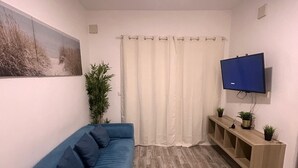 Ein Wohnzimmer mit einem blauen Sofa, einem an der Wand befestigten Fernseher, einer Pflanze und Holzdielen.