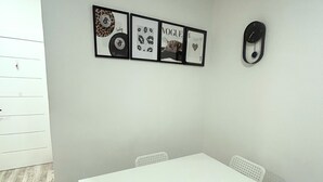 Ein Zimmer mit einem weißen Tisch und Stühlen, einem an der Wand befestigten Bilderrahmen mit verschiedenen Motiven und einer Tür mit Griff.
