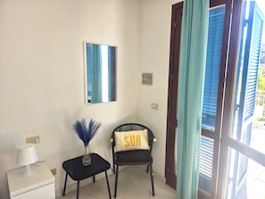 A room with a chair, a small table with a lamp, a mirror, and a window with curtains. - Le Sirene Studio-Escape of Love for 2 with breathtaking views and crystal clear sea (Cavoli)
