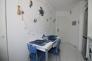 A dining area with a white table, blue chairs, and a decorative net with fish on the wall. - Seafront Terrace & Wi-Fi [600m from station]. (Menton)