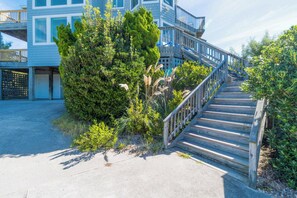 A wooden staircase leading to a building with multiple levels, surrounded by greenery. - Sun Realty pet-friendly oceanside Duck home w/ pool, hot tub & sound views (Duck)