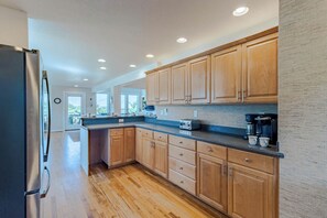 A modern kitchen with wooden cabinets, a stainless steel refrigerator, and a built-in coffee maker. - Sun Realty pet-friendly oceanside Duck home w/ pool, hot tub & sound views (Duck)
