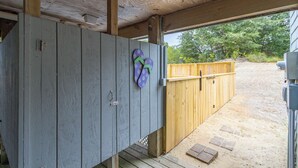 A covered outdoor area with a wooden deck, a wooden fence, and a concrete structure. - Sun Realty pet-friendly oceanside Duck home w/ pool, hot tub & sound views (Duck)