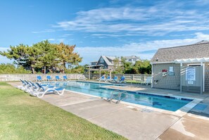 A swimming pool with blue lounge chairs, a covered area, and a building with a sign. - Sun Realty pet-friendly oceanside Duck home w/ pool, hot tub & sound views (Duck)