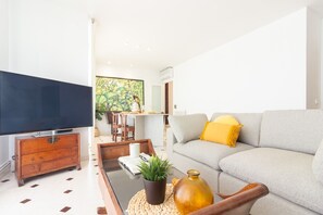 A modern living room with a flat-screen TV, sofa, coffee table, and a dining area in the background.