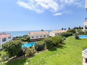 A residential area with a swimming pool, a view of the sea, and a well-maintained lawn.